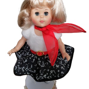 Pu&ograve; includere: Bambola vintage con capelli biondi, indossa un top bianco, una gonna nera con un motivo bianco e una sciarpa rossa. La bambola ha un fiocco rosso e una cintura rossa con fibbia dorata. La bambola &egrave; su un supporto bianco.