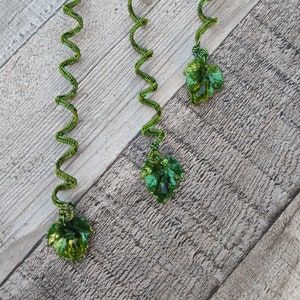May include: Three green wire hair coils, each featuring a spiral design and a dangling green leaf-shaped charm at the bottom. The wire is wrapped in a tight, textured pattern, and the leaves have a glossy, translucent finish with visible veins.