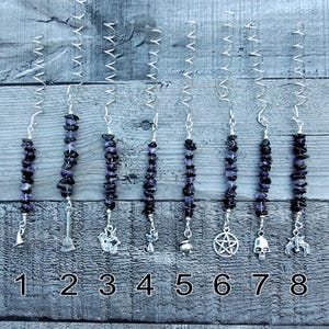 May include: Nine amethyst crystal charms with silver hanging charms. The charms include a witch's hat, a broom, a cat, a cauldron, a star, a pentagram, a skull, and a unicorn. The charms are numbered 1 through 9.