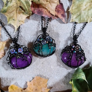 May include: Three wire-wrapped pendants with purple and green stones. Each pendant features a black wire design with small glass beads and flowers.