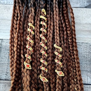 May include: Close-up of brown and blonde braids with gold and red beaded hair jewelry. The jewelry is in the shape of a spiral and is wrapped around the braids.