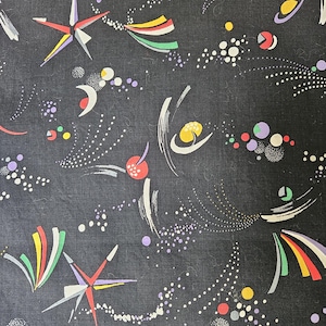 May include: A dark fabric with a repeating pattern of colorful starbursts, dots, and abstract shapes in red, yellow, green, and purple. The design has a retro, space-age feel.