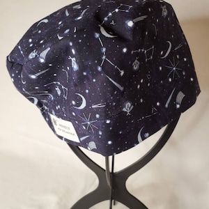 Peut inclure: Un bonnet de travail bleu foncé avec un imprimé de constellations blanches. Le bonnet a une étiquette blanche qui indique "Handmade by The Seamstress".