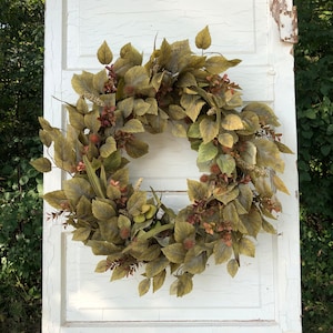 Puede incluir: Una corona de oto&ntilde;o verde y marr&oacute;n con una variedad de hojas y bayas. La corona est&aacute; hecha de materiales artificiales y es perfecta para decorar una puerta o una pared.