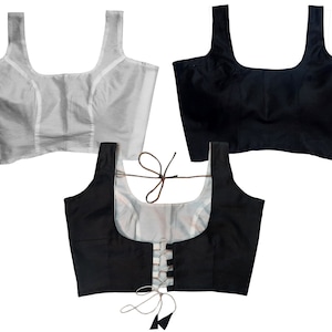 Puede incluir: Tres estilos diferentes de tops cortos negros y blancos. Uno es un top corto negro simple, otro es un top corto blanco simple y el tercero es un top corto negro con un detalle de encaje blanco en la parte delantera.