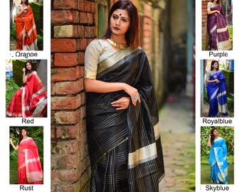 May include: A woman wearing a black and silver striped saree with a white blouse. The saree has a checkered pattern. The woman is standing in front of a brick wall.
