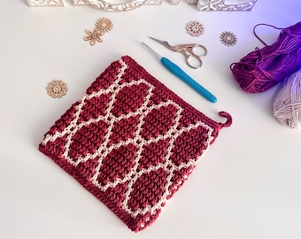 May include: A handmade, square crochet potholder in burgundy and cream. The potholder features a geometric pattern and a small loop for hanging. A blue crochet hook, scissors, and yarn are also visible.