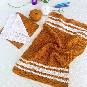May include: A crocheted throw blanket with white stripes on a mustard yellow background. The blanket is folded and lying on a white surface.