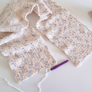 May include: A white and purple crocheted scarf with a purple crochet hook and white yarn.