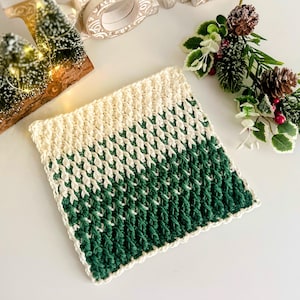 May include: A square, hand-crocheted coaster with a textured pattern. The top half is cream-colored, transitioning to a deep green at the bottom. The coaster is likely made of soft yarn, perfect for protecting surfaces from hot or cold drinks.
