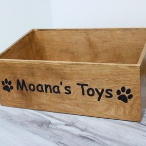 May include: A wooden toy storage box with the words "Moana's Toys" and paw prints on the front.