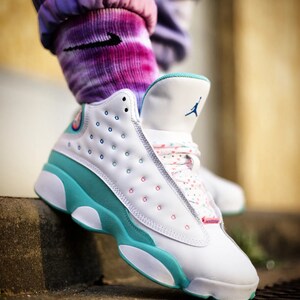 May include: White and turquoise sneakers with a pink and blue polka dot pattern on the laces. The sneakers have a white sole and a turquoise midsole.