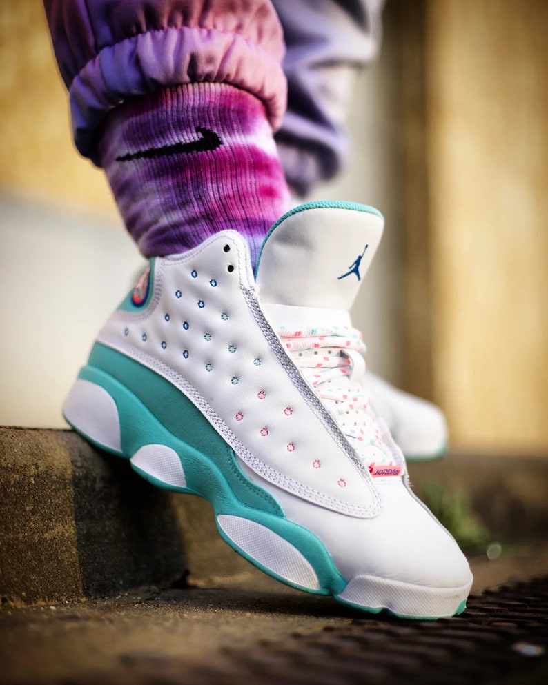 May include: White and turquoise sneakers with a pink and blue polka dot pattern on the laces. The sneakers have a white sole and a turquoise midsole.