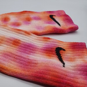 May include: A pair of pink, orange, and white tie-dye socks with a black Nike swoosh logo on each sock.