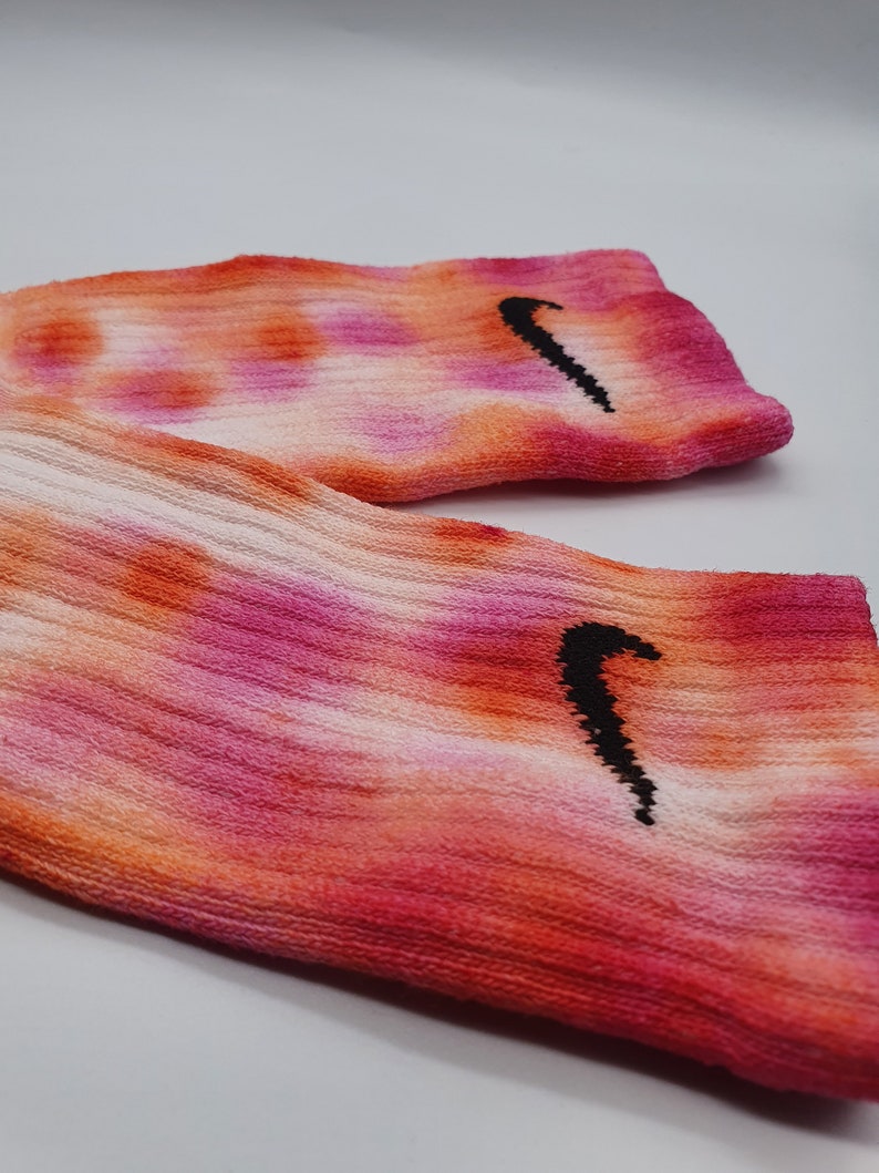 May include: A pair of pink, orange, and white tie-dye socks with a black Nike swoosh logo on each sock.