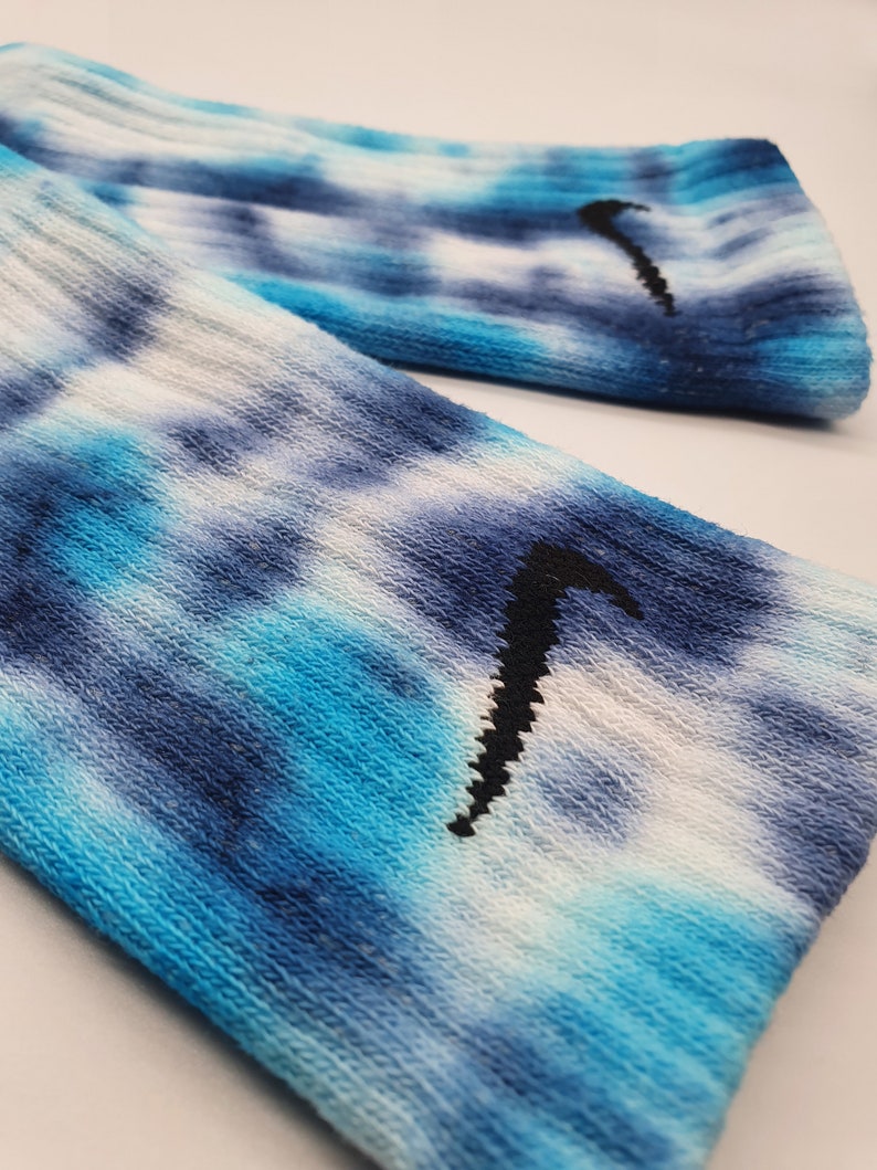 May include: A pair of blue and white tie-dye socks with a black Nike swoosh logo.