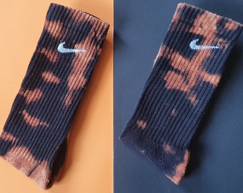 May include: Two pairs of black socks with a white Nike swoosh logo. The socks have a tie-dye pattern with brown and black colors.