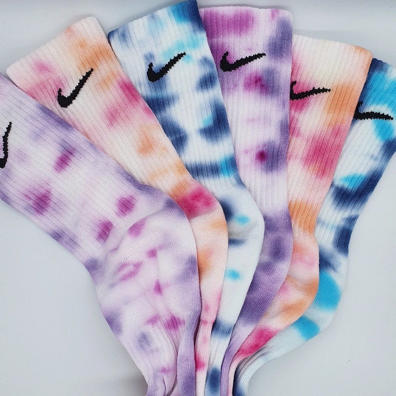 May include: Five pairs of colorful tie-dye socks with a black Nike logo on each sock. The socks are in shades of blue, purple, pink, and orange.