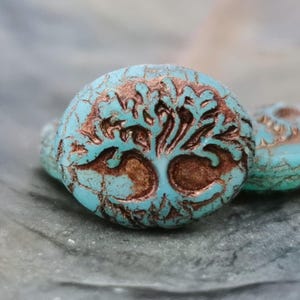 Könnte beinhalten: Nahaufnahme von drei türkisfarbenen, runden Perlen mit einem Lebensbaum-Design. Der Baum ist dunkelbraun und die Perlen haben eine rissige, strukturierte Oberfläche. Die Perlen sind wahrscheinlich für die Schmuckherstellung.