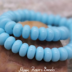 May include: A strand of light blue glass beads. The beads are small and round, and they are strung together on a clear thread.