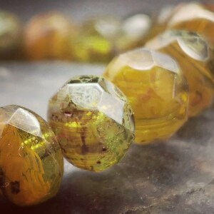 May include: A close-up of a bracelet made of faceted, translucent green and yellow glass beads. The beads are irregularly shaped and have a slightly cloudy appearance.