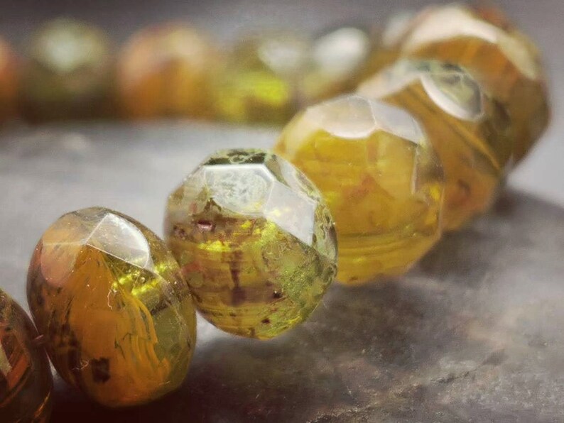 May include: A close-up of a bracelet made of faceted, translucent green and yellow glass beads. The beads are irregularly shaped and have a slightly cloudy appearance.
