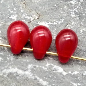 Könnte beinhalten: Drei rote Glasperlen in Tropfenform auf einem goldenen Draht.