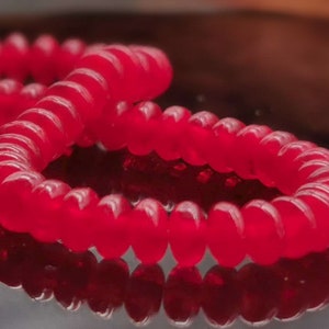 May include: Two red hair ties made of a coiled, flexible material. The hair ties are stacked on top of each other.