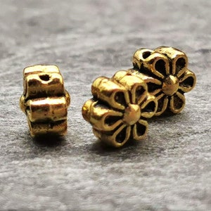 May include: Three gold-colored metal flower-shaped beads. The beads have a raised design and are perfect for jewelry making or crafting.