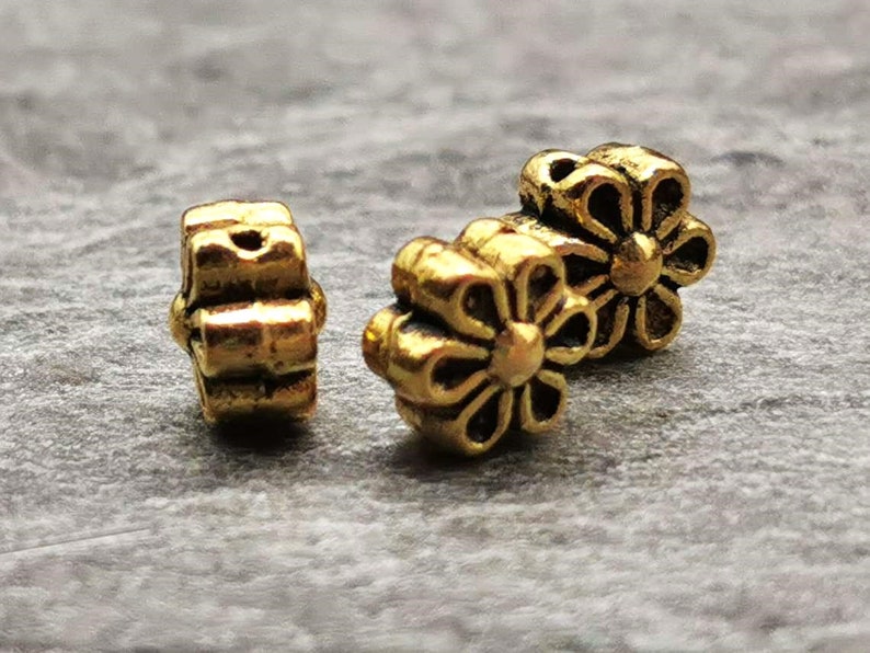 May include: Three gold-colored metal flower-shaped beads. The beads have a raised design and are perfect for jewelry making or crafting.