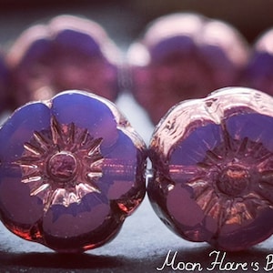 May include: A close-up of a strand of purple glass beads with a flower design. The beads have a metallic sheen and are iridescent.