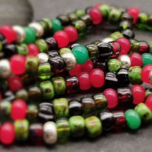 May include: A close-up of a multi-strand beaded bracelet with red, green and black beads. The bracelet also features silver beads.