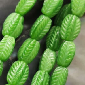 May include: A strand of green glass beads with a leaf design. The beads are oval shaped and have a glossy finish.