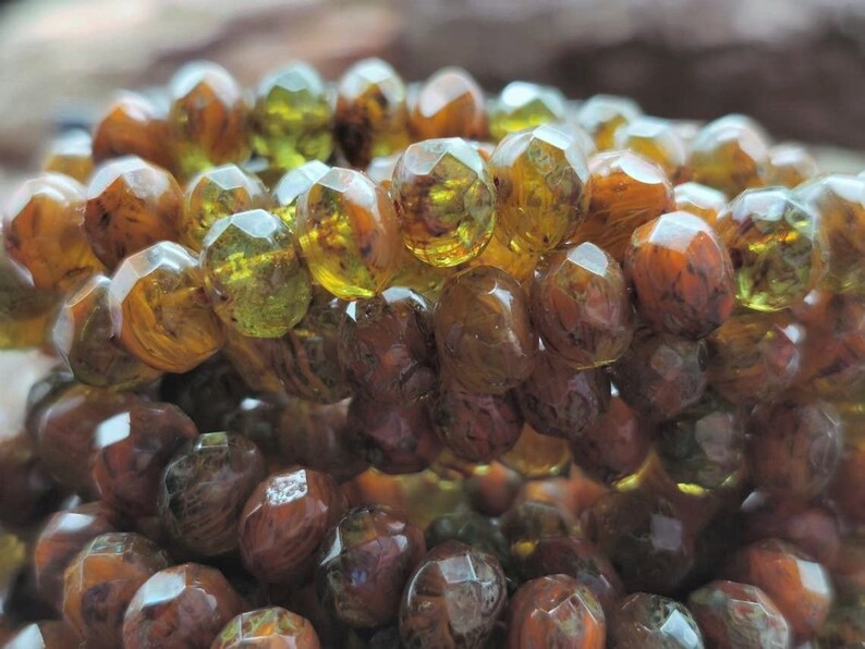 May include: A close-up of a strand of faceted glass beads. The beads are a mix of brown and green with a marbled effect.