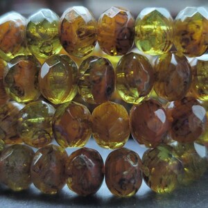 May include: A strand of faceted glass beads in shades of amber and green. The beads have a mottled, marbled appearance.