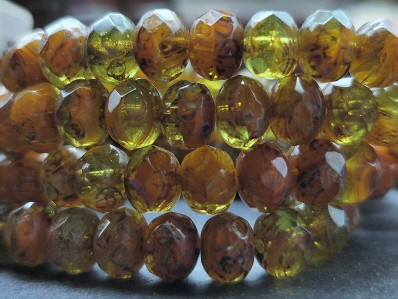 May include: A strand of faceted glass beads in shades of amber and green. The beads have a mottled, marbled appearance.