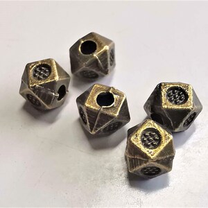 Könnte beinhalten: Fünf antike goldfarbene Metallperlen mit geometrischer Form und einem Loch in der Mitte. Die Perlen haben eine strukturierte Oberfläche und einen leicht abgenutzten Look.