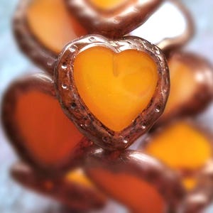 May include: A close-up of a stack of orange heart-shaped charms with a copper-colored metal frame. The charms are stacked on top of each other, creating a layered effect.