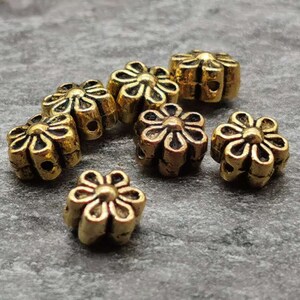 May include: A group of seven gold-colored metal flower-shaped beads. The beads have a raised design and are perfect for jewelry making or crafting.