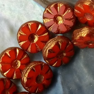 May include: A group of red glass beads with gold accents, each bead features a raised flower design.