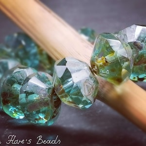 May include: A strand of faceted teal blue glass beads with a light green and white marbled effect. The beads are strung on a wooden skewer.