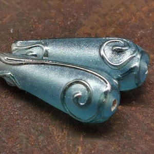 May include: Two light blue glass beads with silver swirls. The beads are teardrop shaped and have a frosted finish.