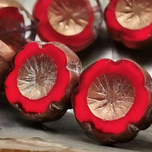 May include: Close-up of red and copper glass beads with a flower-shaped design. The beads have a raised, starburst pattern in the center.