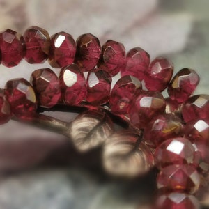 May include: A strand of deep red faceted glass beads. The beads are strung together and have a shiny, reflective surface.
