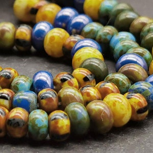 Könnte beinhalten: Eine Strähne bunter Glasperlen mit einem Mix aus blauen, gelben und grünen Tönen. Die Perlen haben einen marmorierten, gefleckten Effekt, der einen einzigartigen und auffälligen Look erzeugt.