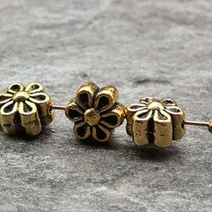 May include: Three gold-colored metal flower-shaped beads with a raised design. The beads are strung on a wire.