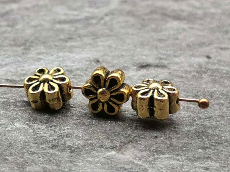 May include: Three gold-colored metal flower-shaped beads with a raised design. The beads are strung on a wire.