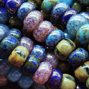Op de afbeelding: Een close-up van een verscheidenheid aan kleurrijke glazen kralen. De kralen zijn rond en hebben een gevlekt of gemarmerd uiterlijk. Sommige kralen hebben een metallic glans.