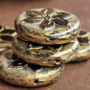 May include: Close-up of several gold and black flower-shaped beads. The beads are stacked, showcasing their detailed floral design. The beads have a metallic finish, adding a touch of elegance. These beads are ideal for jewelry making.