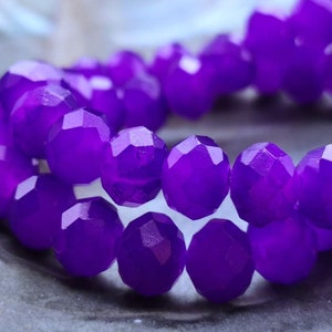May include: A strand of purple faceted glass beads. The beads are round and have a shiny finish.